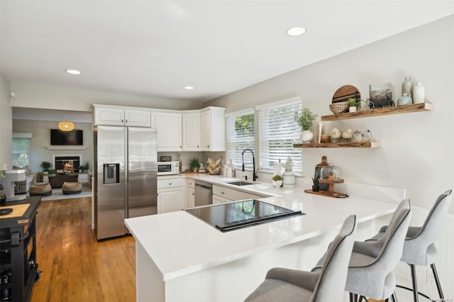 kitchen with kitchen peninsula, a kitchen breakfast bar, stainless steel appliances, sink, and white cabinetry