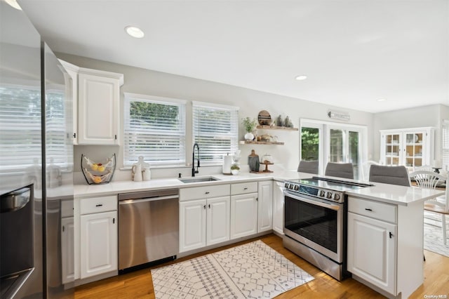 kitchen with kitchen peninsula, appliances with stainless steel finishes, sink, white cabinets, and light hardwood / wood-style floors