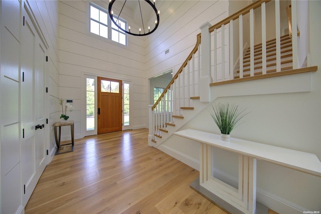 entrance foyer with wooden walls, light wood-type flooring, a high ceiling, and an inviting chandelier