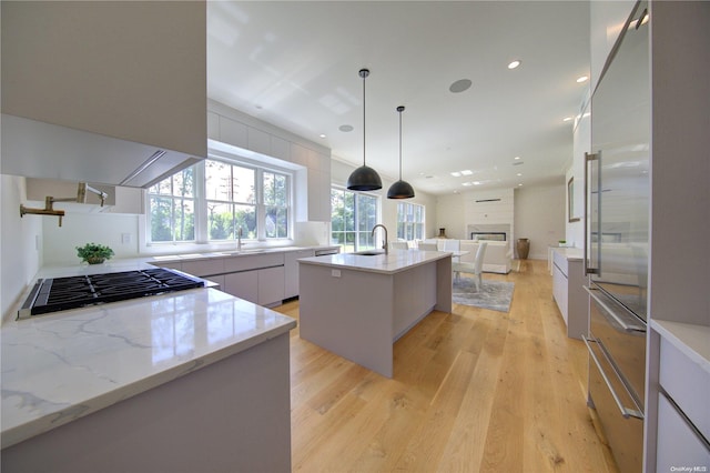 kitchen featuring sink, stainless steel appliances, hanging light fixtures, an island with sink, and light wood-type flooring