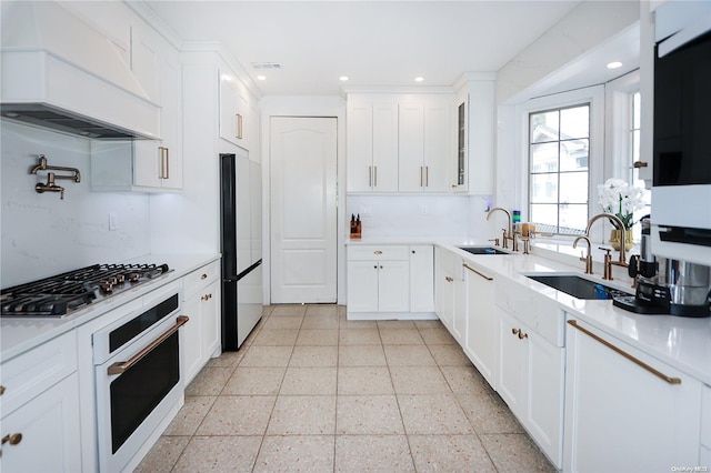 kitchen with custom exhaust hood, white cabinetry, sink, and appliances with stainless steel finishes