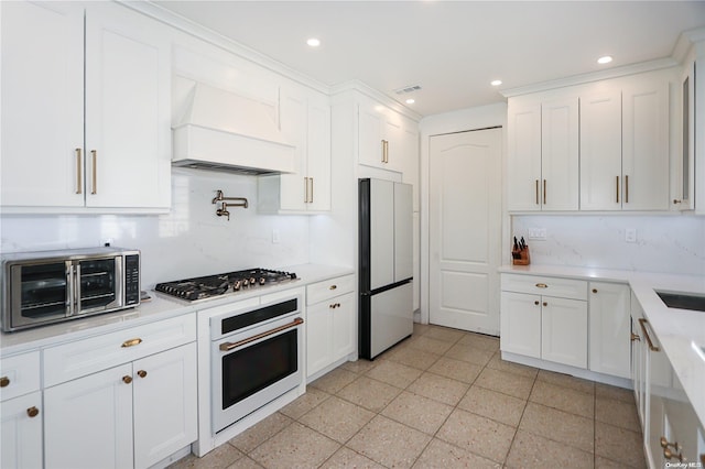 kitchen with white cabinets, decorative backsplash, custom range hood, and appliances with stainless steel finishes