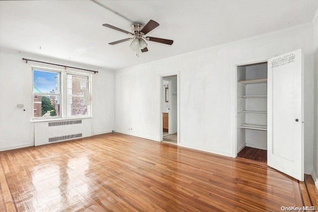 unfurnished bedroom with radiator, ornamental molding, ceiling fan, hardwood / wood-style flooring, and a closet