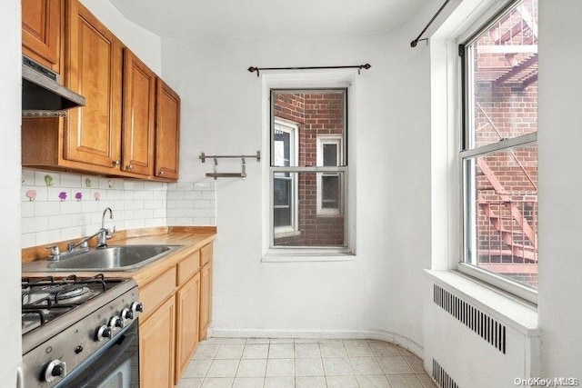 kitchen featuring sink, radiator heating unit, light tile patterned floors, backsplash, and stainless steel stove