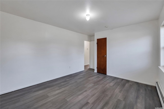 spare room featuring baseboard heating and dark hardwood / wood-style flooring