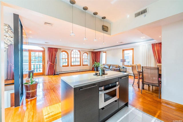 kitchen with pendant lighting, stainless steel oven, a raised ceiling, and light hardwood / wood-style flooring