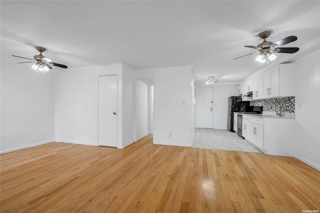 kitchen featuring light wood-type flooring, tasteful backsplash, black fridge, stainless steel range, and white cabinetry