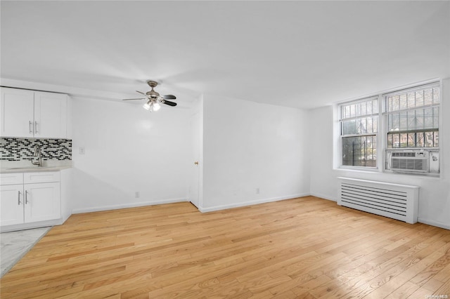 unfurnished living room featuring cooling unit, sink, ceiling fan, light wood-type flooring, and radiator heating unit