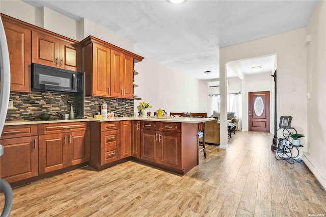 kitchen with backsplash, kitchen peninsula, light hardwood / wood-style floors, a breakfast bar area, and black appliances