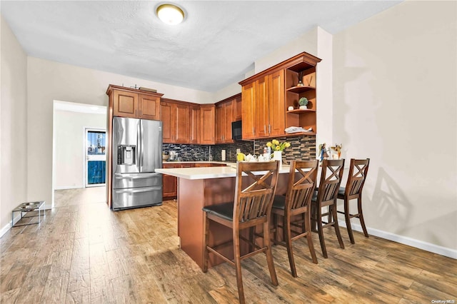 kitchen featuring kitchen peninsula, stainless steel fridge, backsplash, light hardwood / wood-style floors, and a breakfast bar area