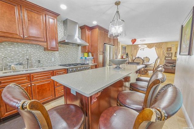 kitchen with a center island, wall chimney exhaust hood, stainless steel appliances, sink, and decorative light fixtures