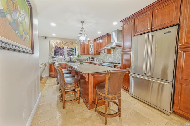 kitchen featuring a breakfast bar, wall chimney exhaust hood, decorative backsplash, appliances with stainless steel finishes, and light stone counters