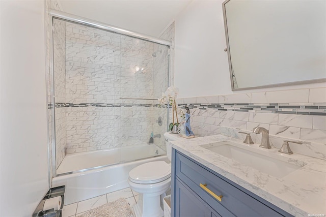 full bathroom featuring tile patterned floors, bath / shower combo with glass door, toilet, vanity, and tile walls