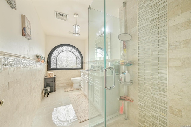 bathroom with tile patterned floors, toilet, tile walls, and a shower with shower door