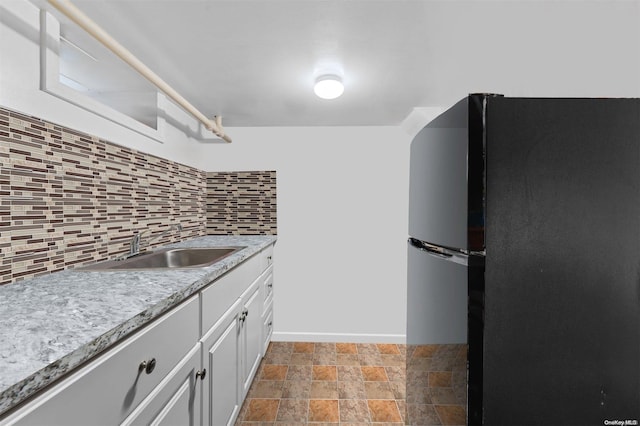 kitchen with tasteful backsplash, black fridge, sink, and white cabinets