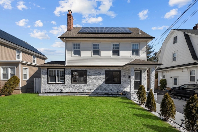 view of front of property featuring a shingled roof, solar panels, stone siding, a chimney, and a front lawn