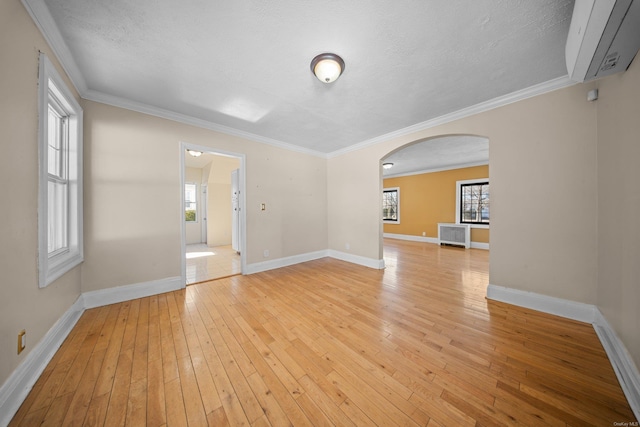 unfurnished room featuring baseboards, arched walkways, ornamental molding, a textured ceiling, and light wood-type flooring