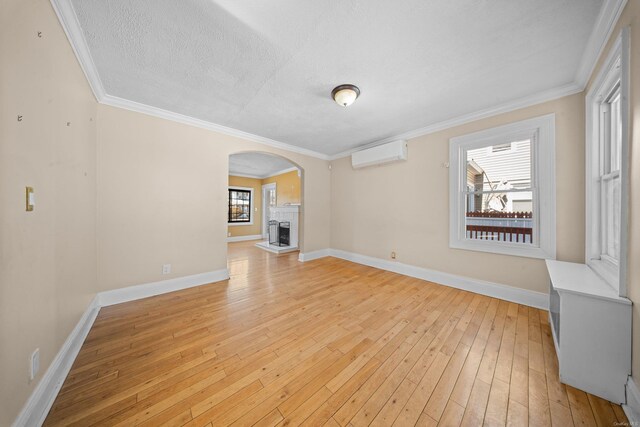 unfurnished living room featuring an AC wall unit, a fireplace with raised hearth, light wood-style flooring, and baseboards