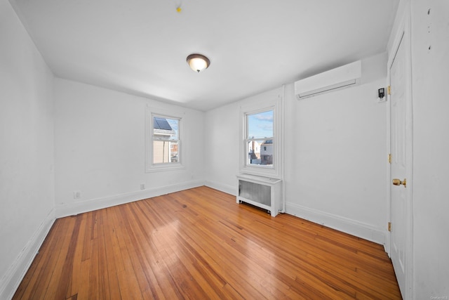 spare room featuring radiator, a wall unit AC, baseboards, and hardwood / wood-style flooring