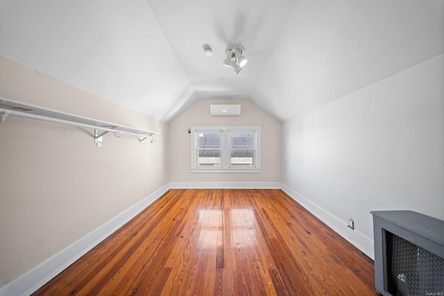 additional living space with wood-type flooring, baseboards, vaulted ceiling, and a wall mounted air conditioner