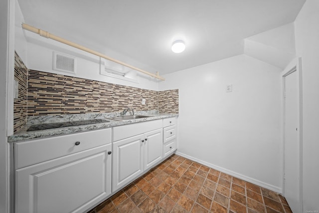 kitchen featuring black electric stovetop, tasteful backsplash, visible vents, white cabinetry, and a sink