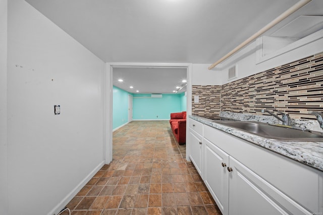 kitchen with visible vents, white cabinets, a sink, light countertops, and backsplash