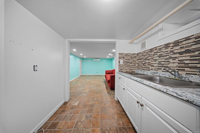 kitchen with a sink, visible vents, baseboards, white cabinets, and tasteful backsplash