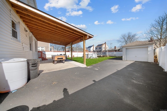 view of patio / terrace with a garage, an outbuilding, fence, and driveway