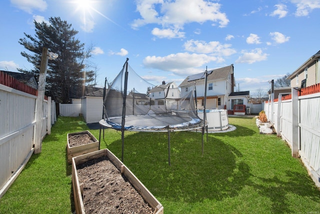 view of yard with a trampoline, a fenced backyard, and a vegetable garden