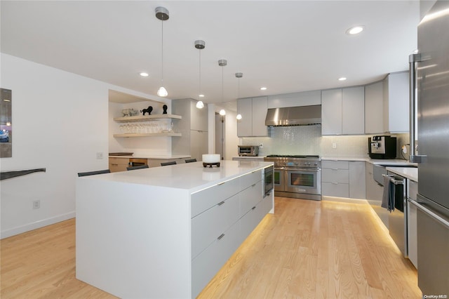 kitchen featuring stainless steel appliances, wall chimney range hood, gray cabinets, a kitchen island, and hanging light fixtures