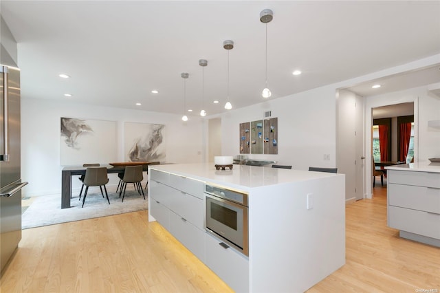 kitchen with a kitchen island, light hardwood / wood-style floors, decorative light fixtures, and appliances with stainless steel finishes