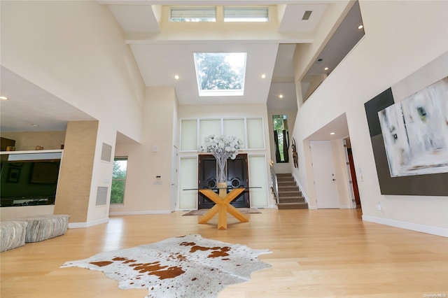 foyer entrance featuring a skylight, light hardwood / wood-style flooring, a towering ceiling, and a healthy amount of sunlight