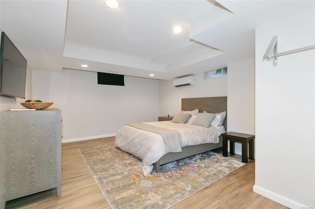 bedroom with hardwood / wood-style floors, a tray ceiling, and a wall mounted AC