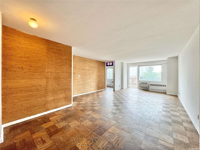 unfurnished living room with a textured ceiling, radiator, and wooden walls