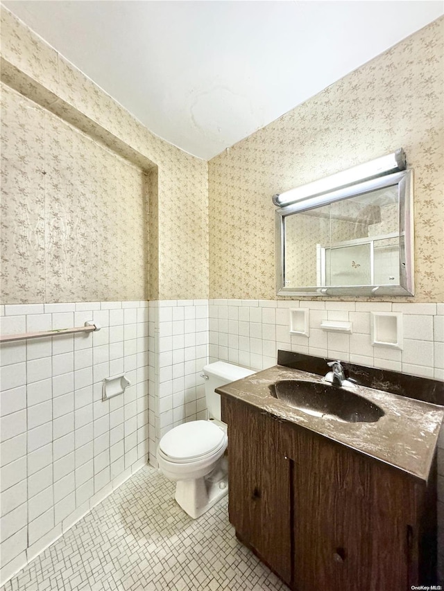 bathroom with tile patterned flooring, vanity, toilet, and tile walls