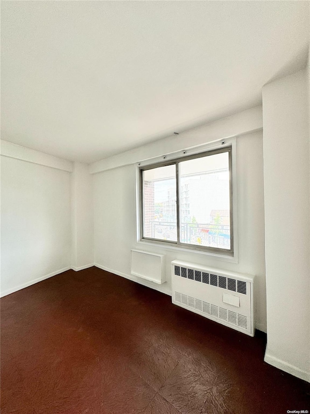 spare room featuring dark carpet and radiator