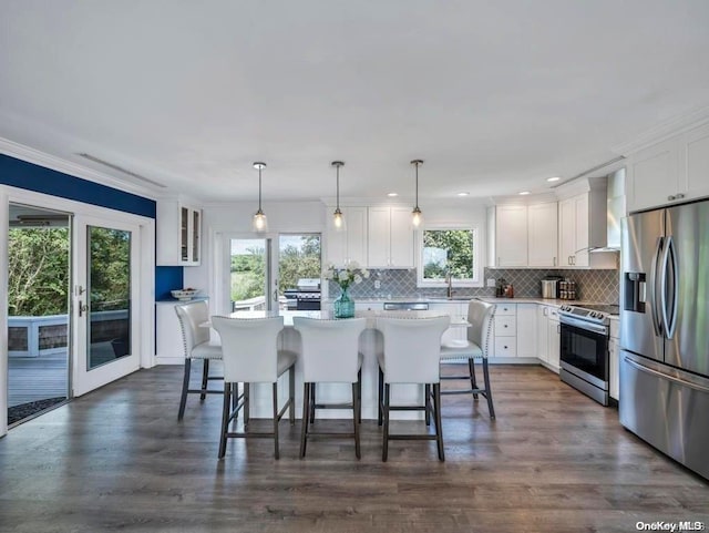 kitchen with white cabinets, wall chimney range hood, stainless steel appliances, and hanging light fixtures