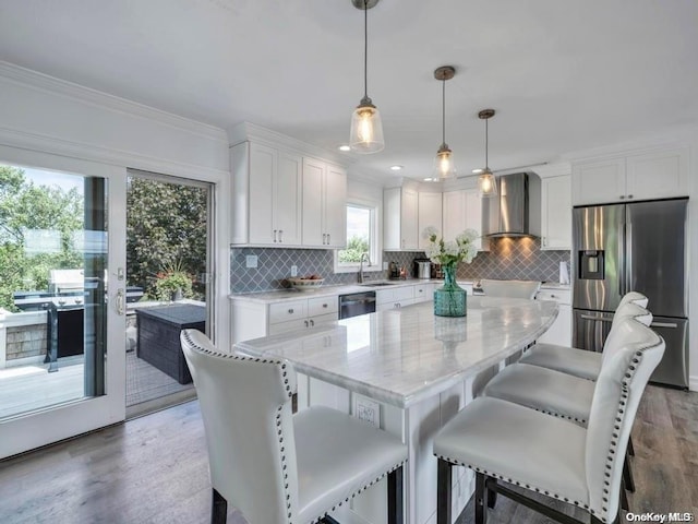 kitchen with appliances with stainless steel finishes, wall chimney range hood, wood-type flooring, decorative light fixtures, and white cabinets