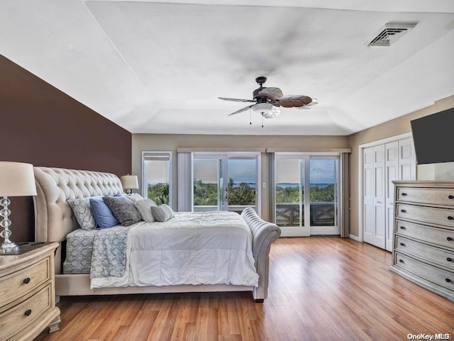 bedroom featuring access to outside, ceiling fan, a tray ceiling, and light hardwood / wood-style floors