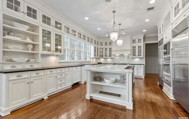 kitchen with dark hardwood / wood-style flooring, stainless steel appliances, a kitchen island with sink, pendant lighting, and white cabinetry