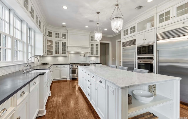 kitchen with a center island, sink, built in appliances, decorative backsplash, and decorative light fixtures