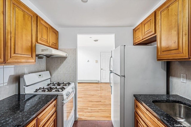 kitchen with decorative backsplash, light hardwood / wood-style floors, dark stone countertops, and white appliances