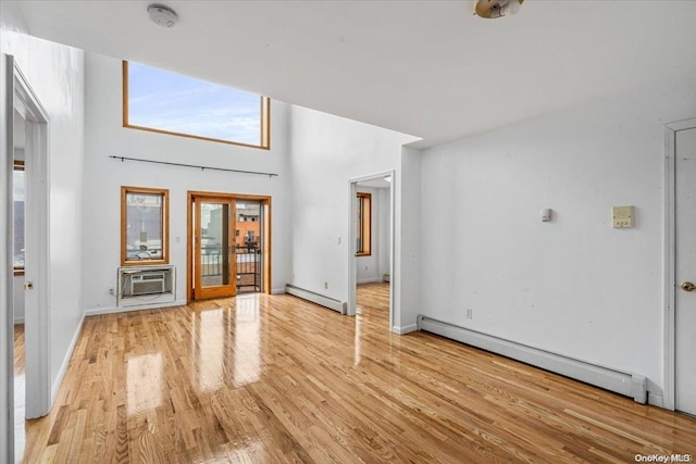 unfurnished living room with a wall mounted air conditioner, light wood-type flooring, baseboard heating, and a towering ceiling