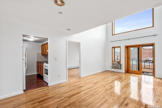 unfurnished living room with a baseboard heating unit, a wall mounted AC, and light hardwood / wood-style flooring