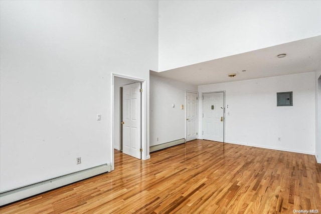 spare room with electric panel, light hardwood / wood-style flooring, a baseboard radiator, and a high ceiling