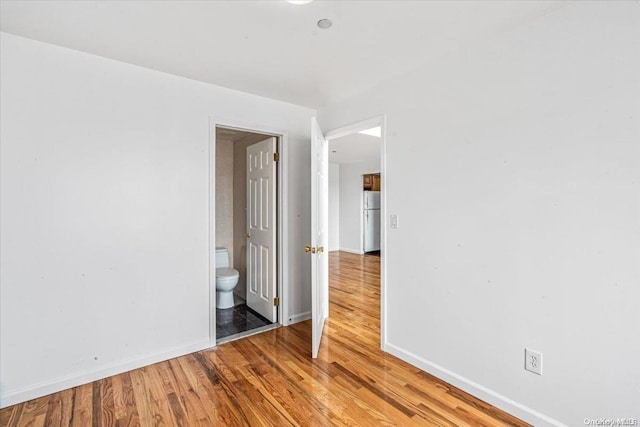 unfurnished bedroom featuring refrigerator, wood-type flooring, and ensuite bath