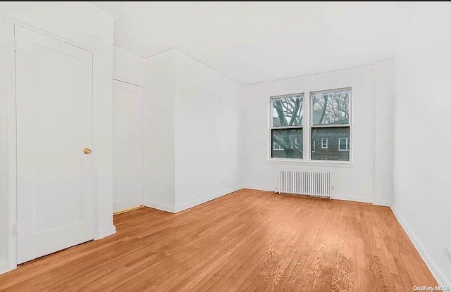 unfurnished room featuring radiator and light hardwood / wood-style flooring