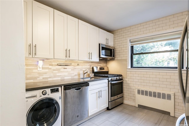 kitchen with sink, radiator heating unit, washer / dryer, white cabinetry, and stainless steel appliances