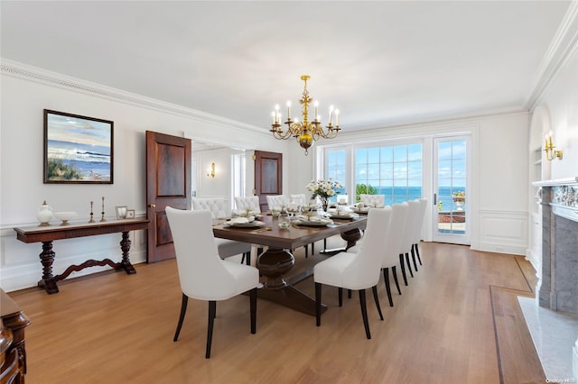 dining space featuring a notable chandelier, crown molding, a fireplace, a water view, and light wood-type flooring