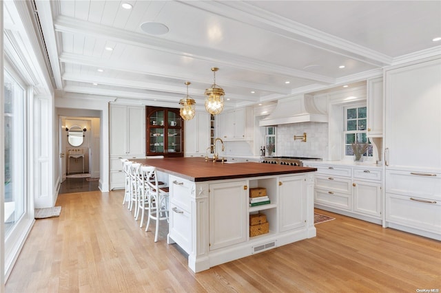 kitchen with wood counters, a center island with sink, white cabinets, and plenty of natural light